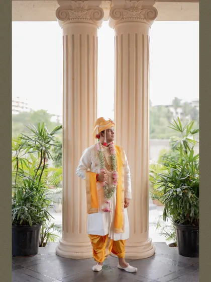 A full-length portrait of the groom standing majestically between two large pillars, looking regal in his wedding outfit.