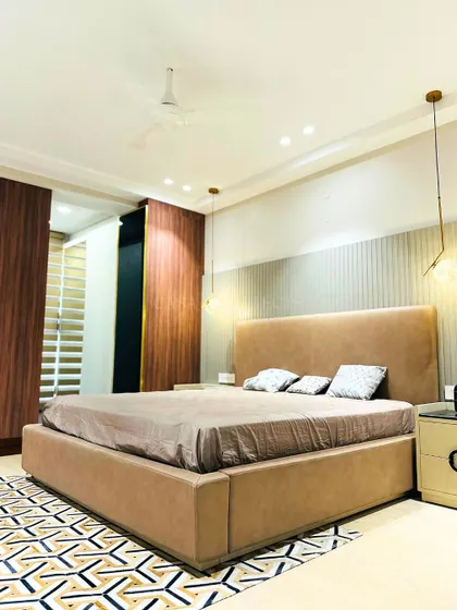 This bedroom features a large, comfortable bed with a leather-like upholstery and a striking geometric rug. The combination of wood, metal, and fabric textures adds depth to the design.