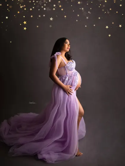 Wishing on a star for her little one. This creative portrait features the mom-to-be in a lavender gown, looking up at a sky of golden stars.
