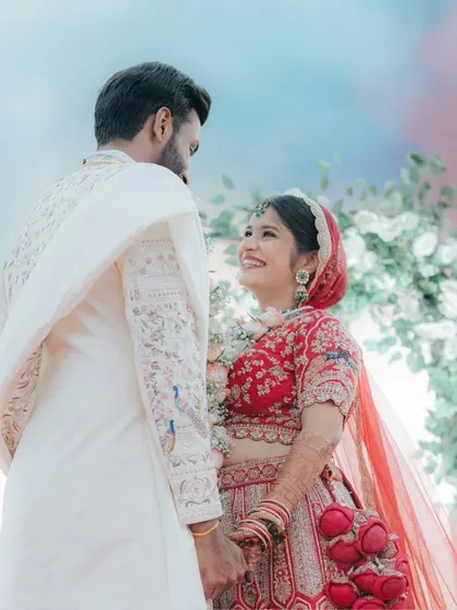 A beautiful low-angle shot of Aboli and Harsh during their Varmala ceremony, with a colourful sky behind them. The bride's joyful smile is priceless.