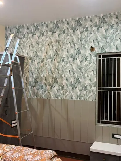 A bedroom during installation, showing a green leaf pattern wallpaper being applied. The half-wall wainscoting provides a nice contrast to the botanical print above.