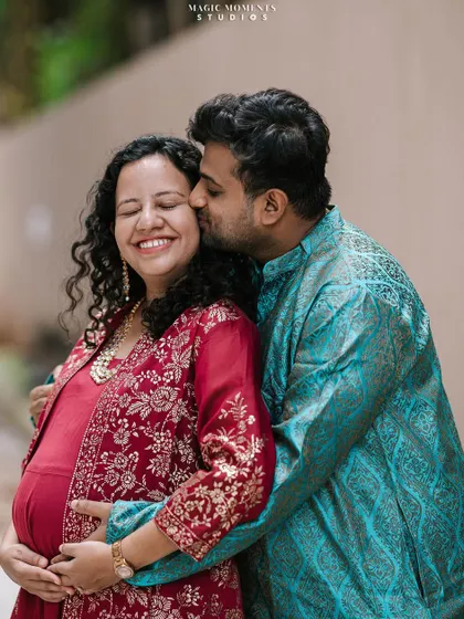 A sweet kiss and a happy smile. This candid shot captures the genuine affection between the couple during their maternity session, dressed in beautiful traditional Indian attire.