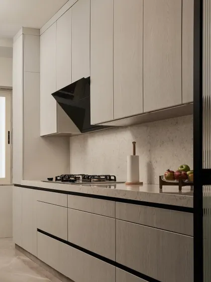The kitchen features a clean, handle-less design with light wood-grain laminate. The soft, rounded corners of the countertops are an ergonomic detail that enhances comfort and safety during daily use.