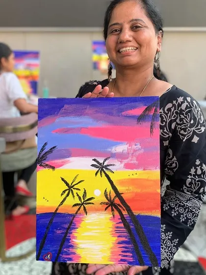 A participant proudly holding up her finished sunset painting. That "I made this!" feeling is what it's all about.