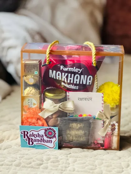 The clear Raksha Bandhan gift box, filled with a mix of modern snacks and traditional elements.