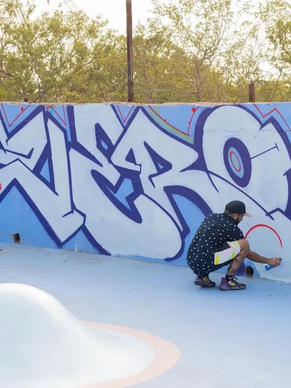 Kneeling down to fill in a large white letter piece at the skatepark. This shows the physical work and attention to detail required.