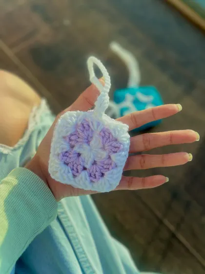 A soft, lilac and white granny square pouch, perfectly sized for AirPods. The handmade construction provides a cushioned layer of protection, and the pastel colors give it a gentle, aesthetic look.