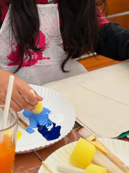 A young artist using a sponge to apply paint to her tote bag. We use a variety of tools to make the process fun and accessible for all ages.