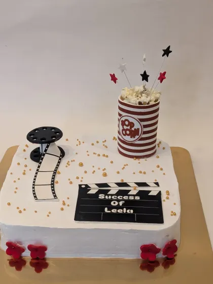 A movie night themed cake. This design features a film reel, a clapperboard for the "Success of Leela," and a bucket of edible popcorn.