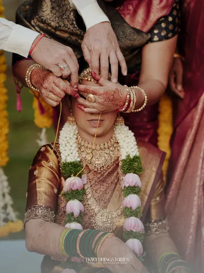 A powerful, artistic shot of a ritual during a South Indian wedding, focusing on the hands and the bride's face.