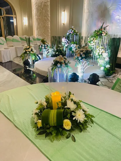 A table centerpiece from the green and white engagement setup. The candle adds a warm glow, complementing the fresh floral arrangement.