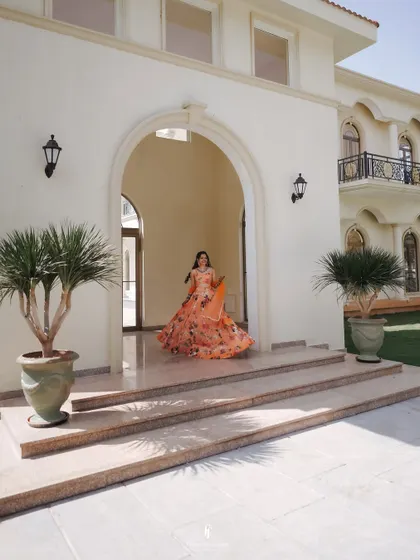 A wide shot of the bride in her floral lehenga, standing at the entrance of a grand villa, ready for her Haldi ceremony to begin.