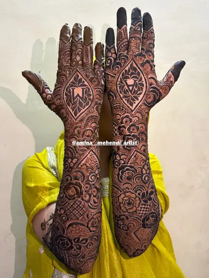A full view of the 'AM' initial mehendi, showing the complete design extending up to the elbows with a mix of floral and traditional patterns.