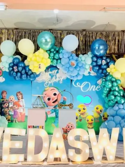 A grand Cocomelon first birthday stage with large marquee letters spelling out the name 'VEDASWI'.