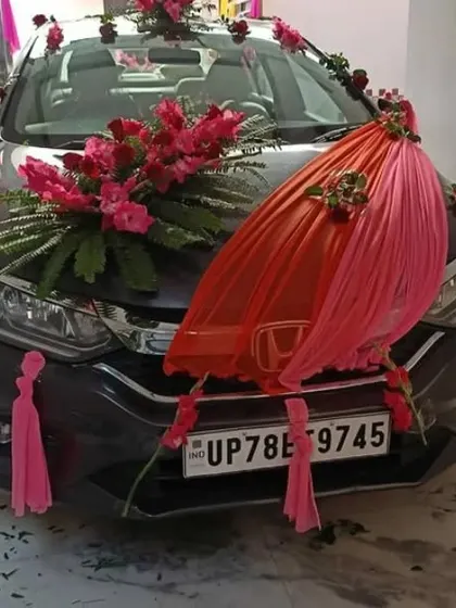 A wedding car decorated with large bouquets of pink flowers and a combination of pink and orange fabric draping on the hood.