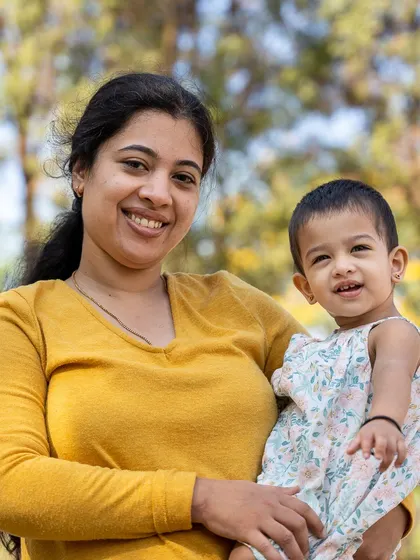 A mother's gentle smile as she holds her little one. This outdoor portrait captures the simple, beautiful bond between a mother and her child. The soft, natural light and blurred background keep the focus entirely on their sweet connection.