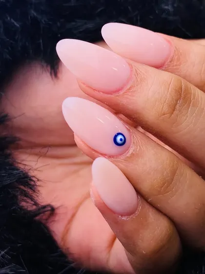 A simple yet meaningful design. This classic nude manicure on almond-shaped nails features a single, tiny evil eye accent, offering a touch of protection and a trendy, minimalist statement.