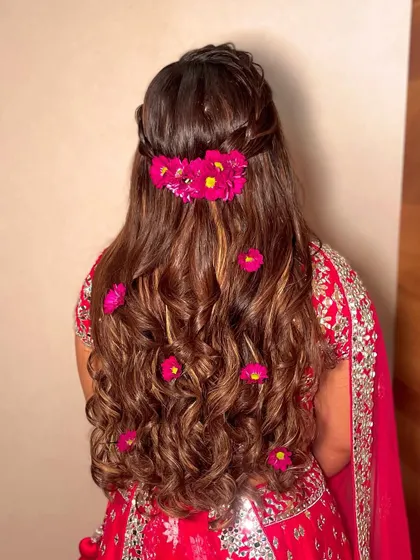 A half-updo with fresh pink flowers scattered through the curls, a perfect look for a Haldi or Mehendi.