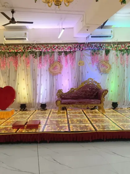 A beautiful engagement stage setup with a floral backdrop, an ornate sofa, and a large heart prop. The colorful lighting creates a romantic mood.