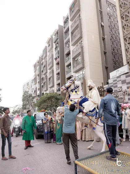 The baraat begins. The groom, dressed in a white sherwani, gets ready to mount the decorated horse for his procession.