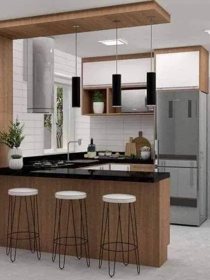 A compact and functional kitchen with a breakfast bar for two. The black countertop and pendant lights contrast nicely with the wood and white cabinets.