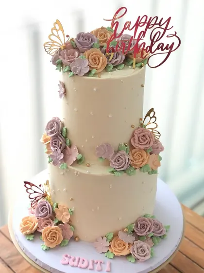 A stunning two-tiered cake in a soft pastel palette, adorned with hand-piped buttercream flowers and gold butterfly accents.