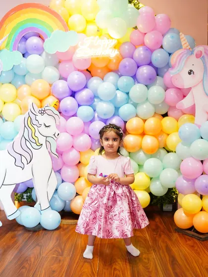 The birthday girl poses in front of her pastel rainbow balloon wall, a beautiful and popular choice for unicorn and magical themes.