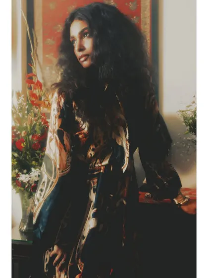 This image from "Roots" uses soft, warm light to create a feeling of nostalgia and introspection. The model's pose against a backdrop of flowers and textiles evokes a sense of home and belonging.