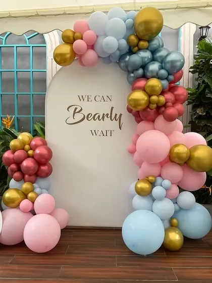 A "We Can Bearly Wait" themed baby shower backdrop. This setup uses a soft color palette of pink, blue, red, and gold balloons, with a clean white arch for the custom message.