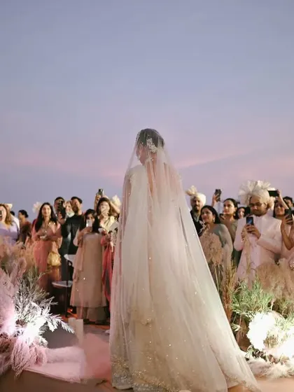 The bride's grand entrance at her sunset beach wedding in Thailand, with guests looking on against the backdrop of the dusky sky.