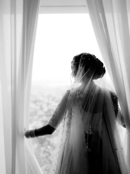 A timeless black and white silhouette of the bride looking out a window. The play of light and shadow creates a classic and artistic bridal portrait.