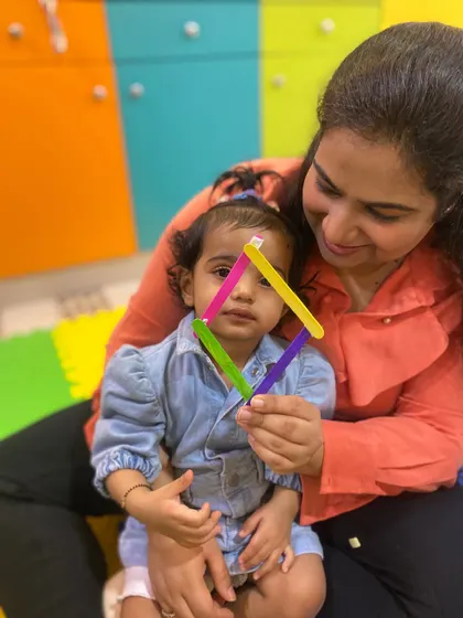 A mother and daughter in our Rajouri Garden class hold up a triangle made from popsicle sticks, a fun way to learn about shapes.