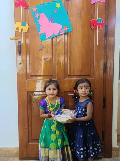 Two adorable friends in their festive best, participating in the Makar Sankranti tradition of sharing sweets.