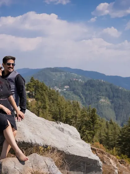 The couple sits together on a rock, looking out at the expansive green and blue mountain ranges. A perfect moment of shared peace and admiration for the view.