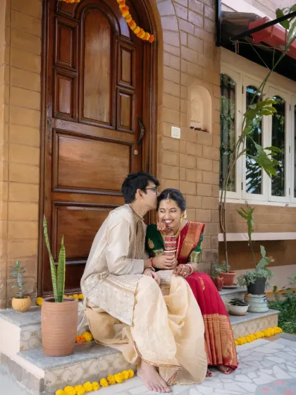 A sweet, candid moment between a couple sitting on their front steps, the groom placing a gentle kiss on her forehead.