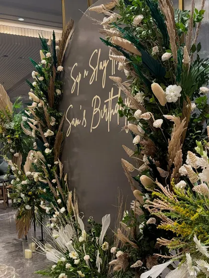A bohemian-themed birthday backdrop for "Sam's Birthday". This design uses a mix of pampas grass, dried palm leaves, and fresh white flowers to create a natural and earthy aesthetic.
