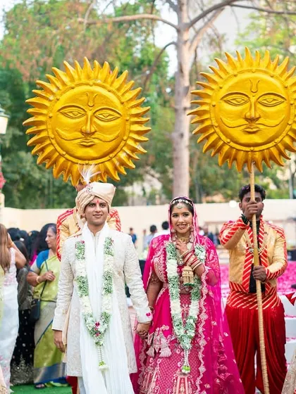 The happy couple walks together, surrounded by dancers and attendants holding golden sun props. This kind of coordinated, themed procession ensures your entry as a couple is a shared, joyous experience.
