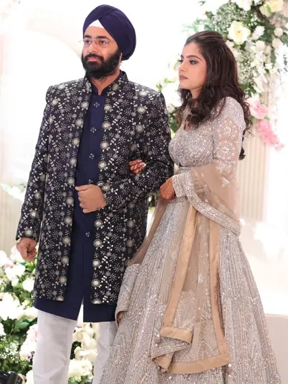 Here is another look at the stunning couple from their sangeet. This view shows how his dark, detailed jacket provides a beautiful contrast to her light, sparkling lehenga, creating a balanced and visually captivating coordinated look as they make their entrance.