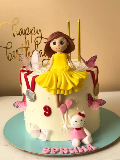 A sweet cake featuring Hello Kitty and a doll topper, decorated with medals and butterflies for a little champion.