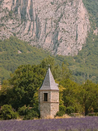 A stone tower stands amidst a lavender field at the base of a mountain in Provence. This image combines architecture and landscape to create a classic, picturesque scene.
