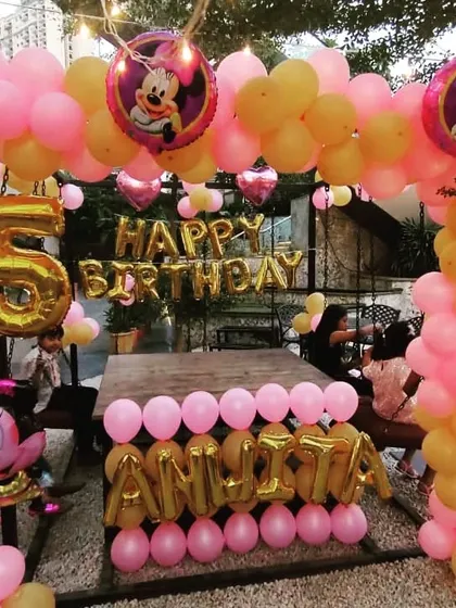 A classic Minnie Mouse theme for a 5th birthday. This outdoor setup includes a pink and gold balloon arch, foil balloons of the character, and the birthday girl's name in large gold letter balloons.