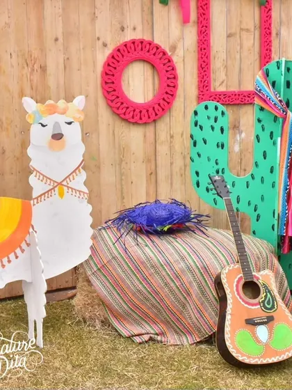 A cute photo spot featuring a llama prop, a cactus, and a guitar, all set against a rustic wooden wall for a fun, fiesta-themed picture.