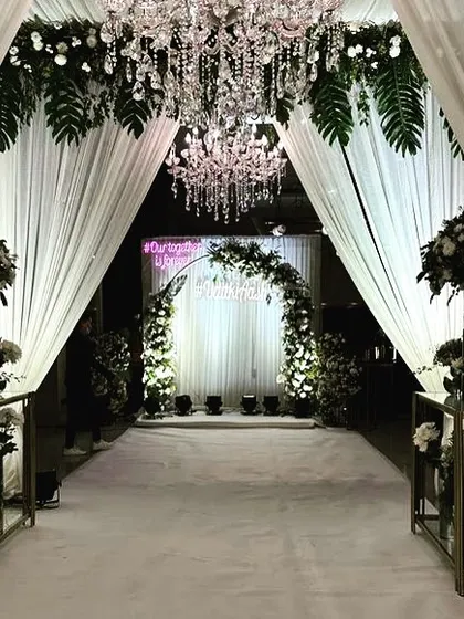 A grand entrance tunnel created with white drapes, hanging greenery, and crystal chandeliers, leading guests to the main event area.