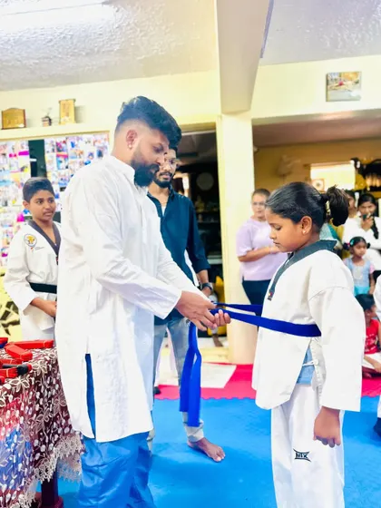 A young girl receives her blue belt, a significant step up in her Taekwondo journey.