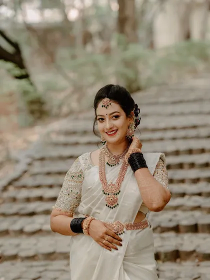 A joyful portrait of a South Indian bride in a white saree, set against a stone staircase. We use natural settings to create timeless and elegant bridal photos.