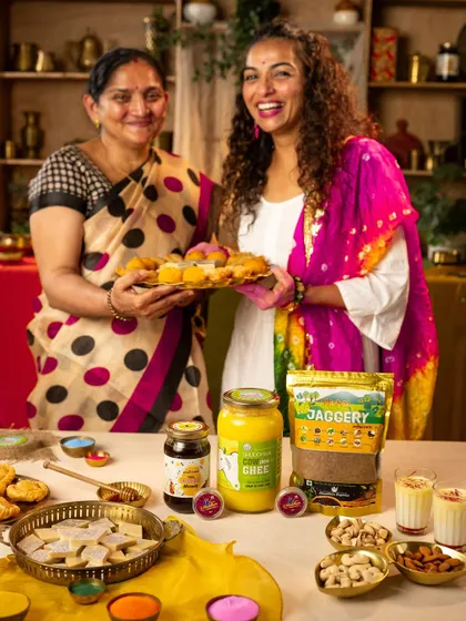 A happy portrait of two women presenting a tray of Holi sweets, with brand products displayed on the table. This is a great example of lifestyle product placement.