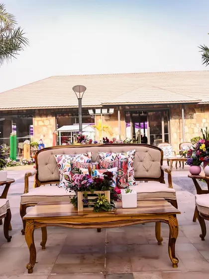 Another seating area from the Rajasthani-themed Mehendi, featuring elegant wooden furniture with colorful printed cushions, blending rustic charm with vibrant accents.