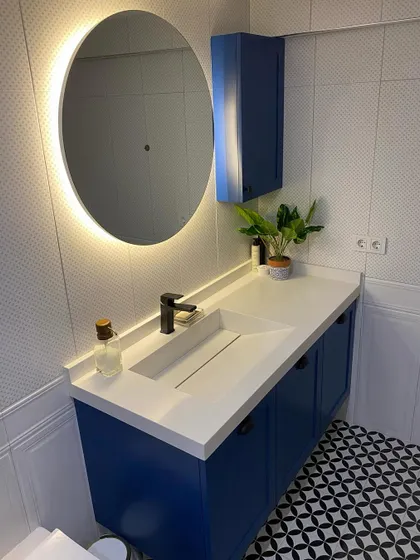 A bold and stylish bathroom design featuring a royal blue vanity, a countertop with an integrated sink, and a striking black-and-white patterned floor. The backlit mirror adds a soft, ambient glow.