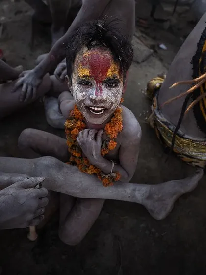 A young boy, his face painted with ash and color, smiles amidst the crowd in Varanasi. Children are an integral part of these ancient traditions, their joy adding another layer to the city's spiritual fabric.
