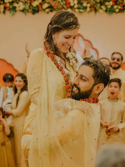 A joyful, candid moment from the Haldi. The groom lifts his bride, both of them covered in turmeric and smiling, a perfect capture of their fun-loving relationship.